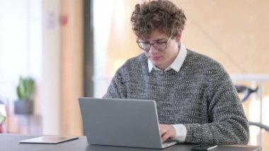 Dizüstü bilgisayarlı yaratıcı genç adam kamerayı işaret ediyor.