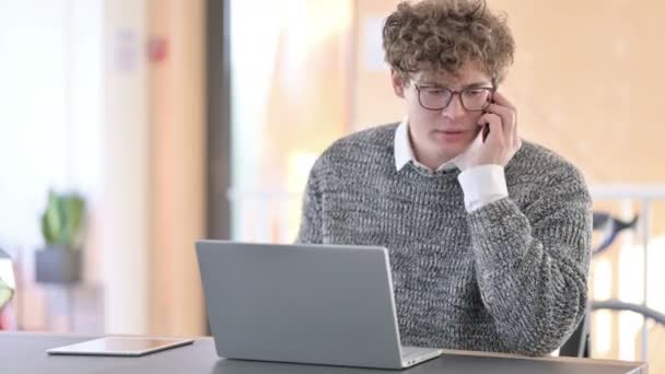 Kreativer junger Mann mit Laptop wütend auf Smartphone bei der Arbeit — Stockvideo