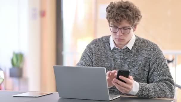 Jovem criativo usando Smartphone e Laptop no trabalho — Vídeo de Stock