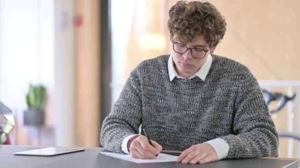 Jonge creatieve jonge man die op papier schrijft op het werk — Stockvideo