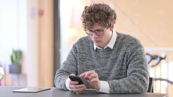 Ongelukkig creatieve jonge man met verlies op Smartphone op het werk — Stockvideo