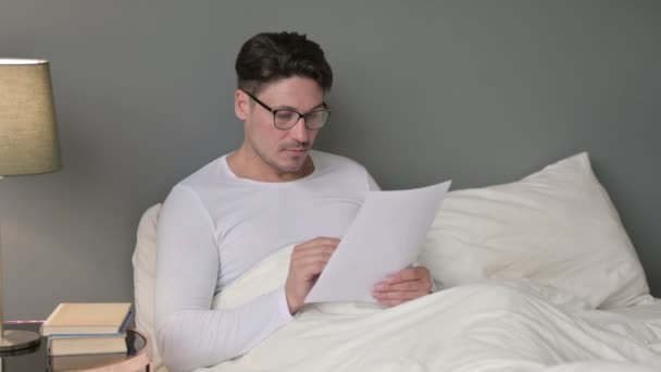Keményen dolgozó középkorú férfi olvasási dokumentumok az ágyban — Stock videók