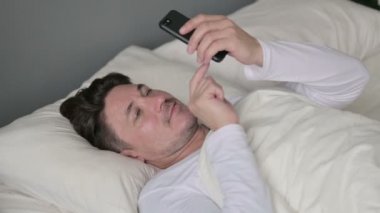 Yatakta Uzanmış Orta Yaşlı Adam 'ın akıllı telefon kullanımı 