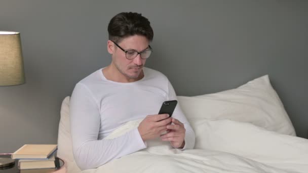 Utilisation du smartphone par un homme sérieux du Moyen Âge au lit — Video