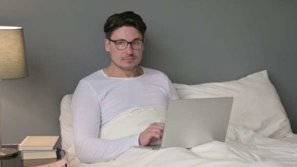 Middeleeuwse man met laptop op zoek naar camera in bed — Stockvideo