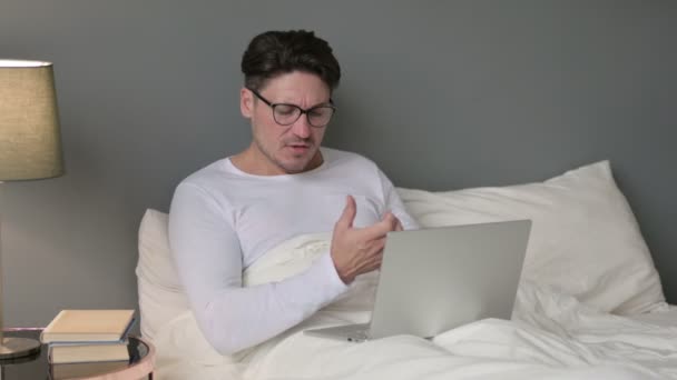 Мужчина среднего возраста с ноутбуком, с болью в запястье в постели — стоковое видео