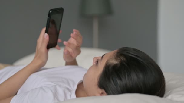 Індійська жінка використовує смартфон лежачи в ліжку — стокове відео