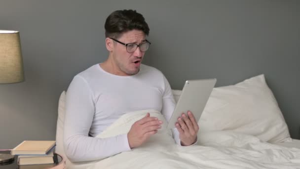 Middelbare leeftijd Man reageert op verlies op tablet in bed — Stockvideo