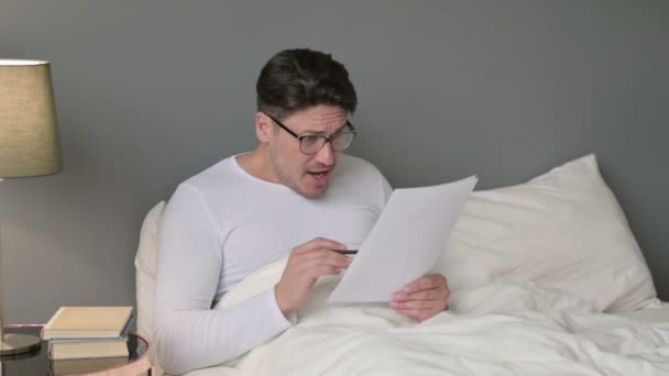 Hombre de mediana edad con documentos que reaccionan a la pérdida en la cama — Vídeos de Stock