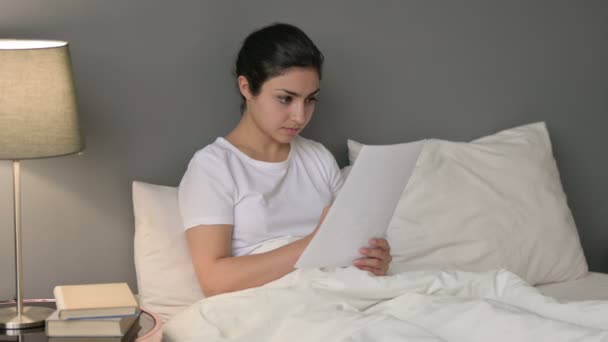 Молодая индийская женщина делает бумажную работу в постели — стоковое видео