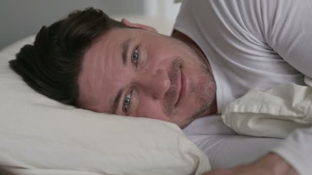 Hombre de mediana edad acostado en la cama sonriendo a la cámara — Vídeos de Stock