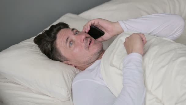 Hombre de mediana edad hablando en Smartphone acostado en la cama — Vídeos de Stock