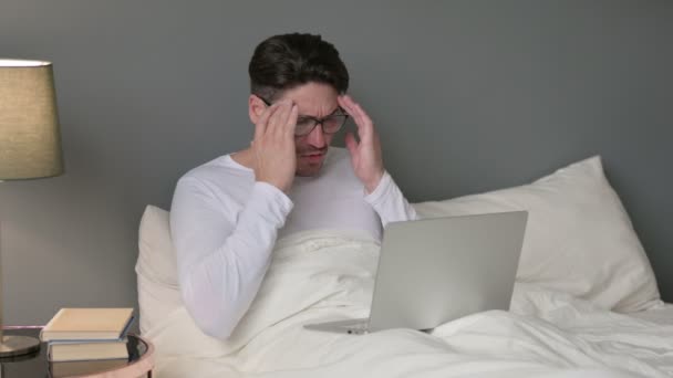 Gestresster Mann mittleren Alters sitzt mit Kopfschmerzen im Bett — Stockvideo