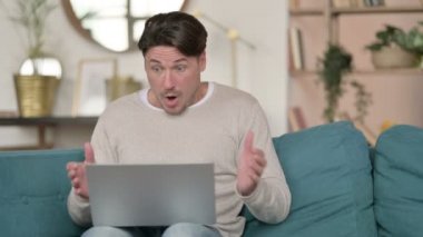 Orta yaşlı adam laptopta, evde kaybına tepki veriyor.
