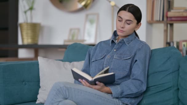 Latina mulher sentada leitura livro no sofá — Vídeo de Stock
