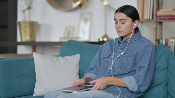 Mujer latina escuchando música en la tableta en el sofá — Vídeos de Stock