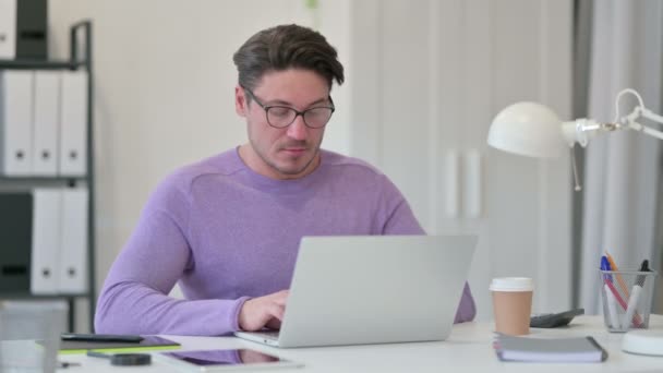 Kreativer Mann mittleren Alters mit Laptop niest im Büro — Stockvideo