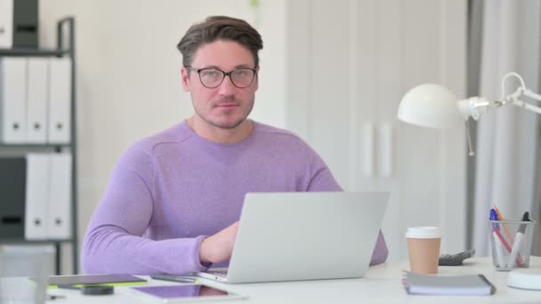 Hombre creativo de mediana edad con el ordenador portátil sonriendo a la cámara — Vídeos de Stock