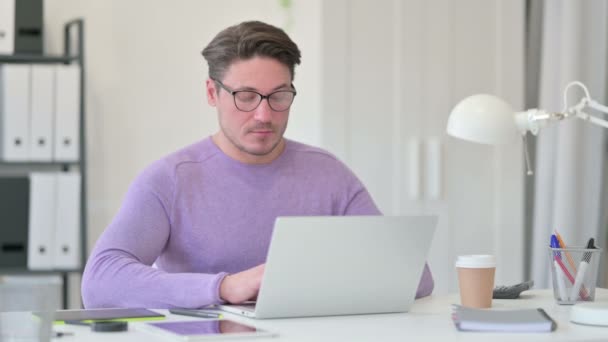 Kreativer Mann mittleren Alters mit Laptop, der auf die Kamera zeigt — Stockvideo