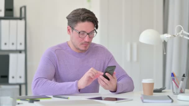 Hombre creativo de mediana edad usando Smartphone en la oficina — Vídeos de Stock