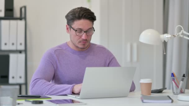 Kreativer Mann mittleren Alters mit Laptop hustet im Büro — Stockvideo