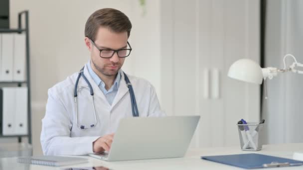 Joven médico masculino trabajando en el ordenador portátil en la oficina — Vídeo de stock