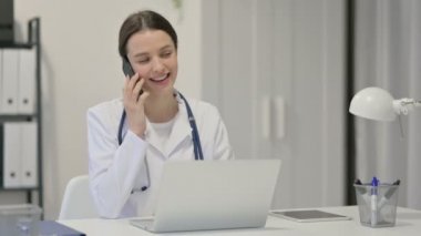 Dizüstü bilgisayarlı genç bayan doktor. Akıllı telefondan konuşuyor. 
