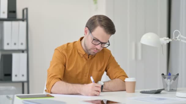 Jonge man die op papier schrijft op kantoor — Stockvideo