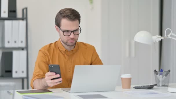 Young Man with Laptop using Smartphone in Office — Stock Video