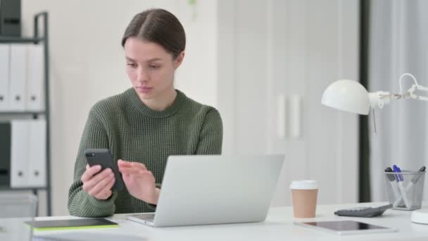 Jonge vrouw met laptop met behulp van Smartphone — Stockvideo