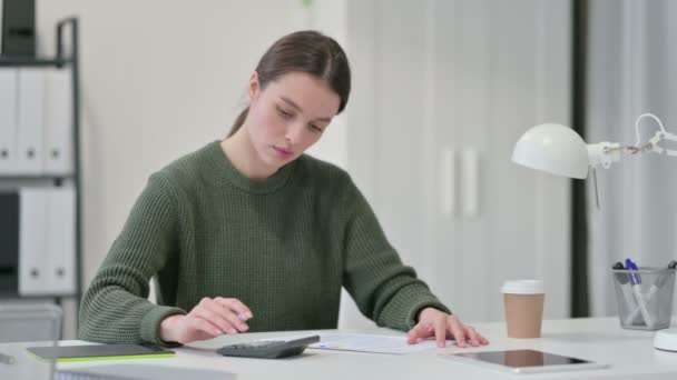 Молодая женщина с помощью калькулятора пишет на бумаге — стоковое видео