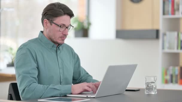 Среднего возраста человек работает на ноутбуке в офисе — стоковое видео