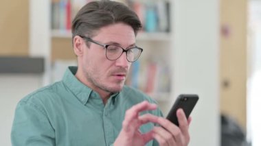 Orta yaşlı adam akıllı telefondan kayboluyor. 