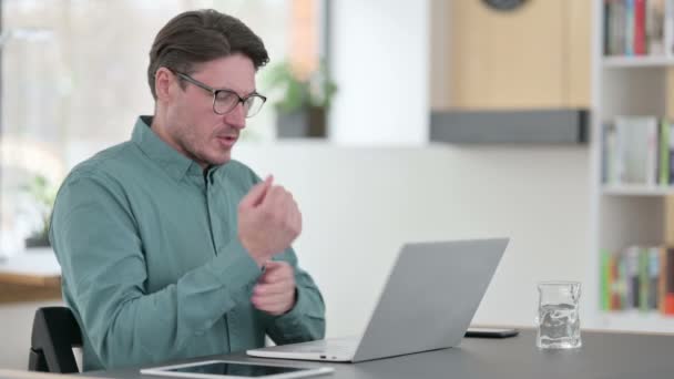 Чоловік середнього віку, який має зап "ясток, працюючи на ноутбуці — стокове відео