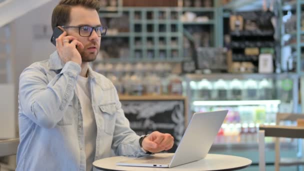 Homem criativo com laptop conversando no telefone — Vídeo de Stock