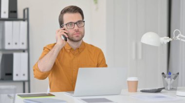 Dizüstü bilgisayarlı genç adam Smartphone 'da konuşuyor 