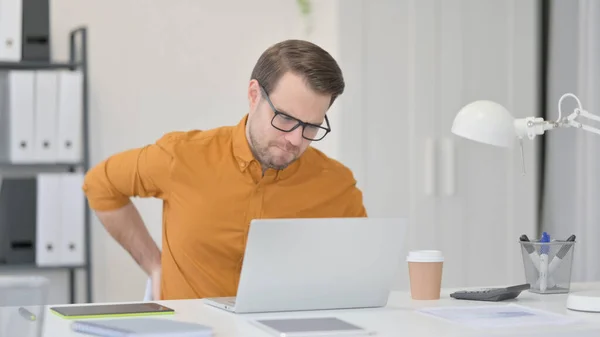 Jeune homme avec ordinateur portable ayant mal au dos au bureau — Photo