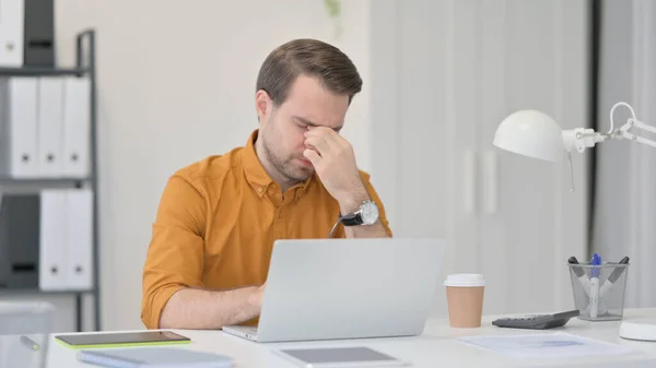 Mladý muž s notebookem s bolestí hlavy v kanceláři — Stock fotografie