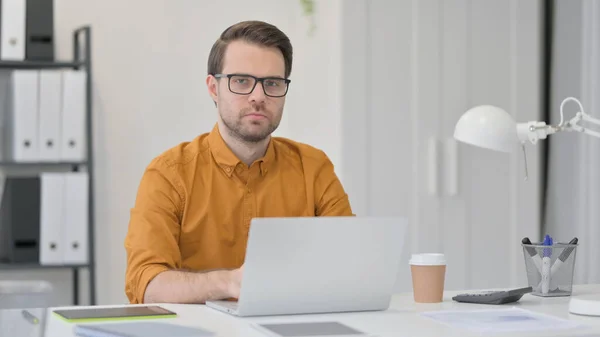 Jeune homme avec ordinateur portable regardant la caméra — Photo