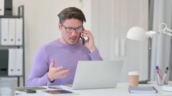 Sint mellomgammel mann med laptop som snakker på Smartphone – stockfoto