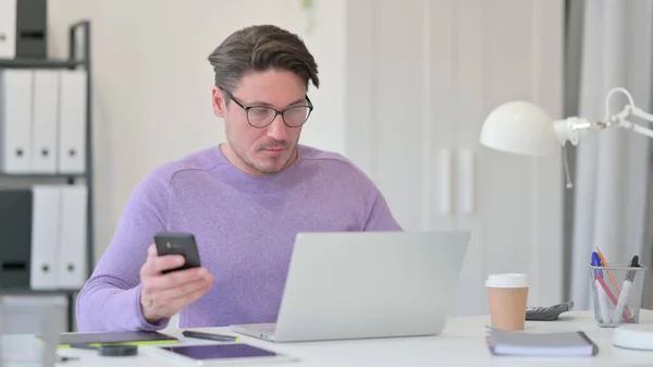 Mann mittleren Alters mit Laptop und Smartphone im Büro — Stockfoto