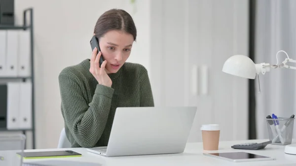 スマートフォンで話すラップトップの若い女性 — ストック写真