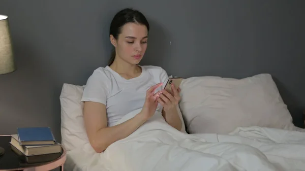Використання смартфона молодою жінкою в ліжку — стокове фото