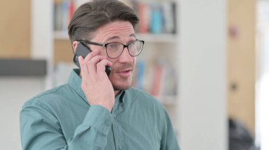 Orta yaşlı adam telefonda konuşuyor. 