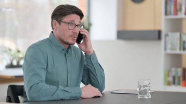 Orta yaşlı adam iş yerinde telefonla konuşuyor. 