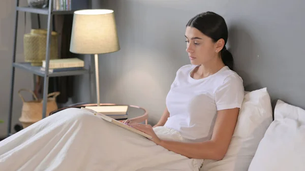 Молода Латинська жінка читає книгу в ліжку — стокове фото