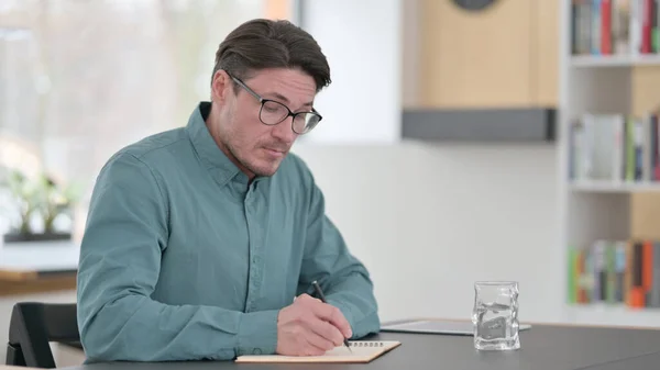 Mann mittleren Alters schreibt bei der Arbeit auf Papier — Stockfoto