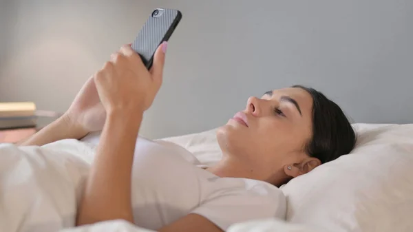 Латинська жінка використовує смартфон у ліжку — стокове фото