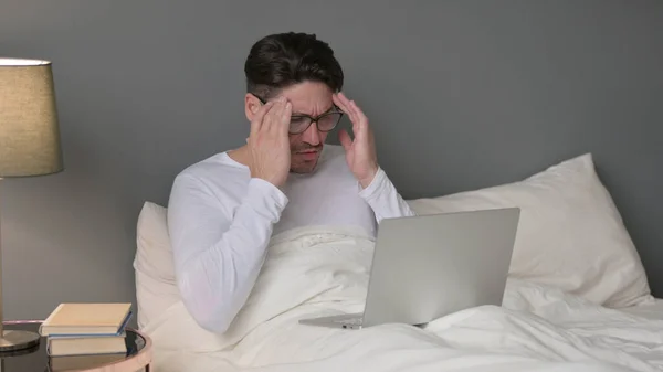 Людина середнього віку з головним болем за допомогою ноутбука в ліжку — стокове фото