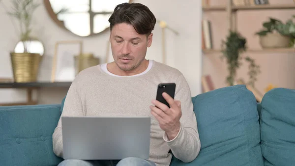 Hombre de mediana edad usando Smartphone y Laptop en casa —  Fotos de Stock